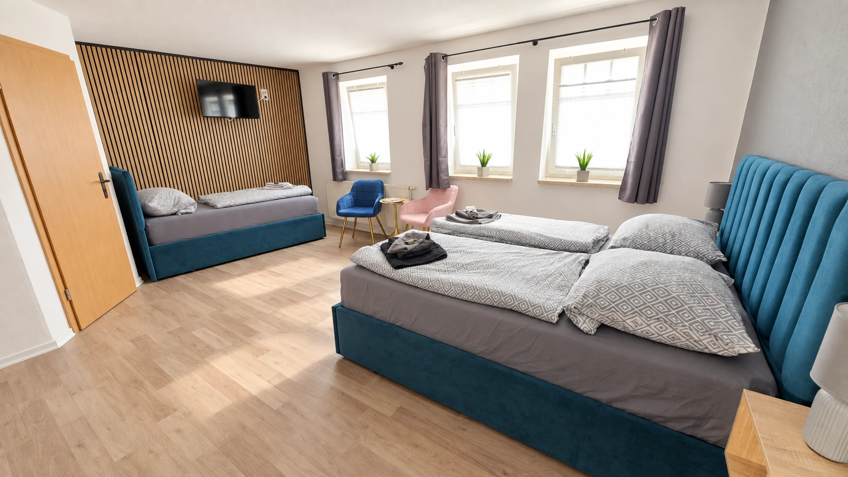 Dreibettzimmer im Hotel Hasa mit petrolfarbenem Samt-Tagesbett und Holzlamellenwand.
